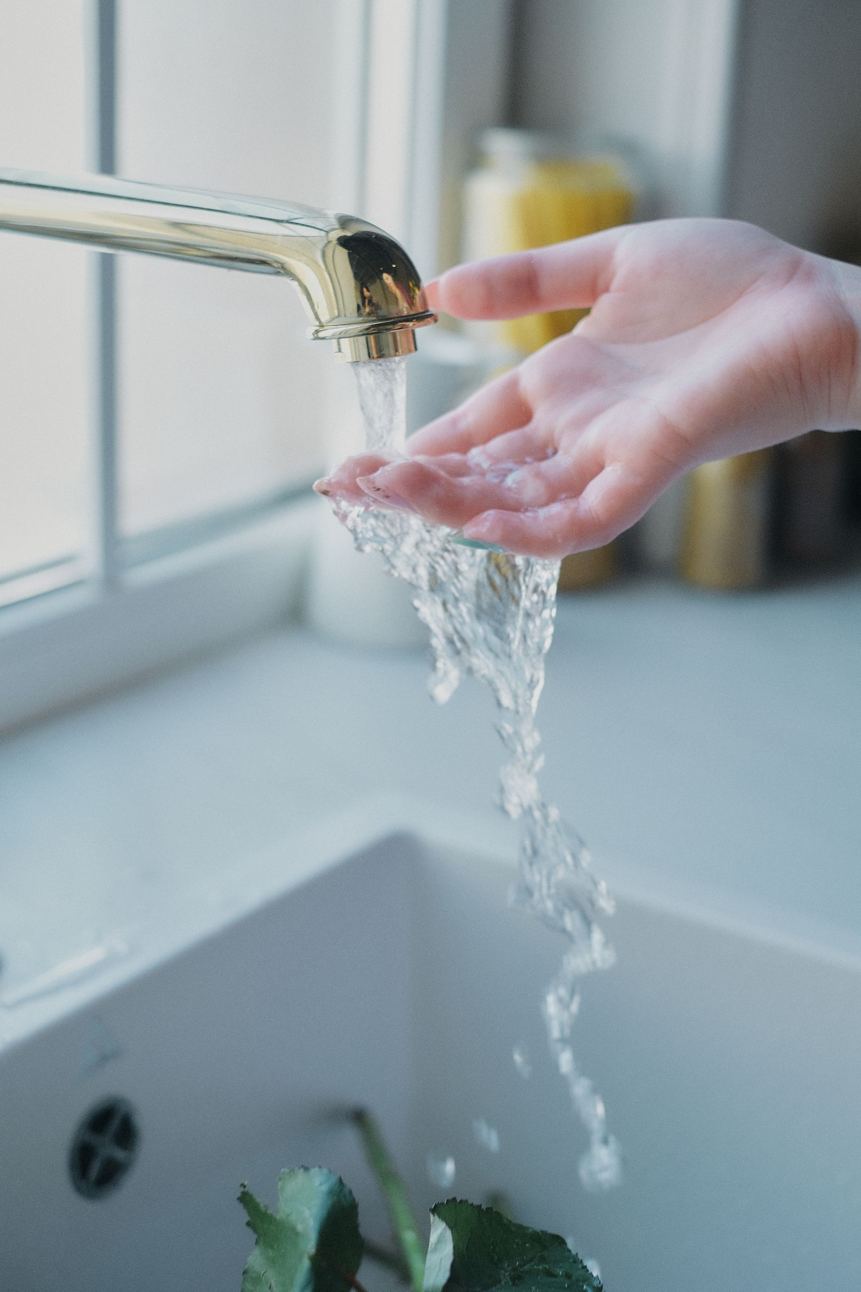 A soft focus image of water flowing over a hand under a kitchen tap, creating a serene ambiance.